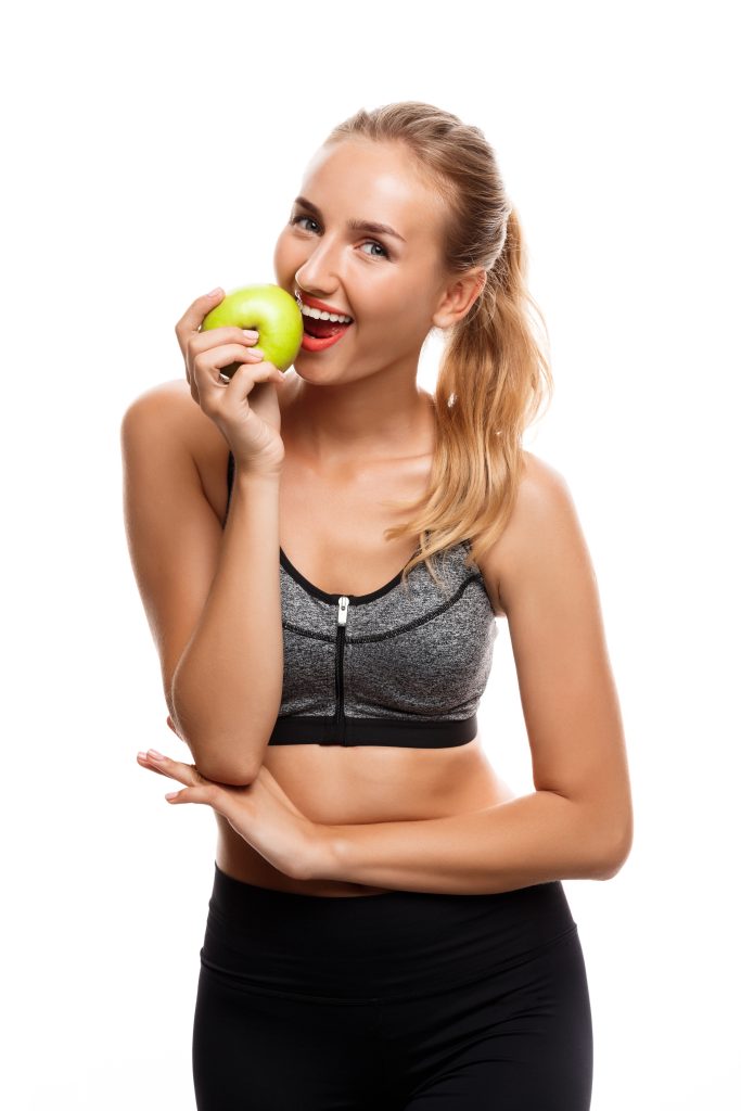 Beautiful sportive girl posing, holding apple over white background.