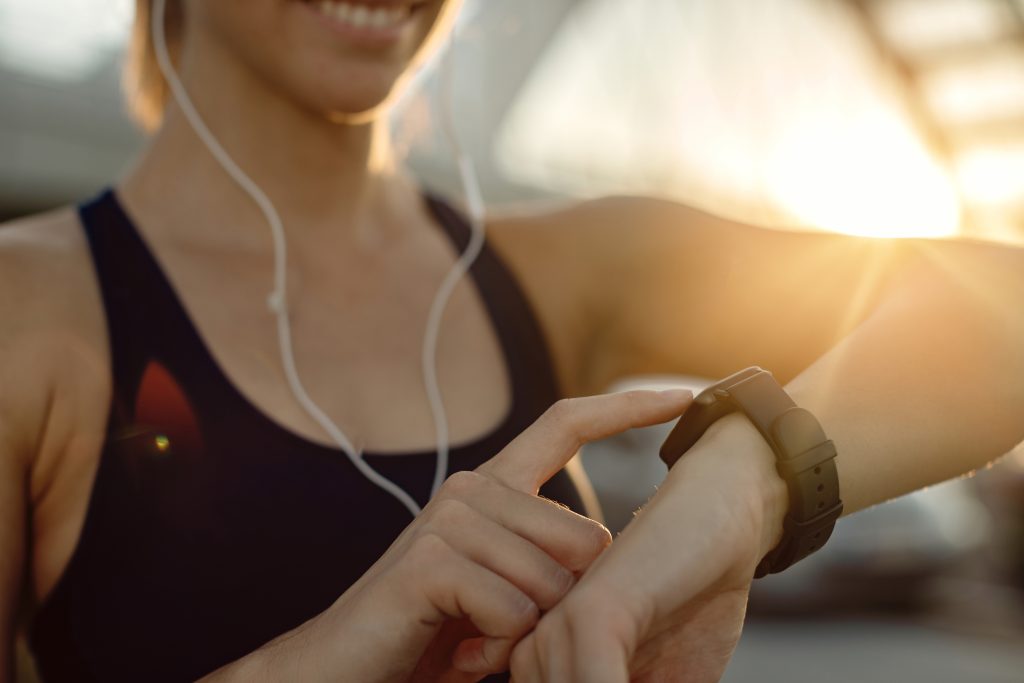 Close-up of athletic woman using fitness tracker at sunset.