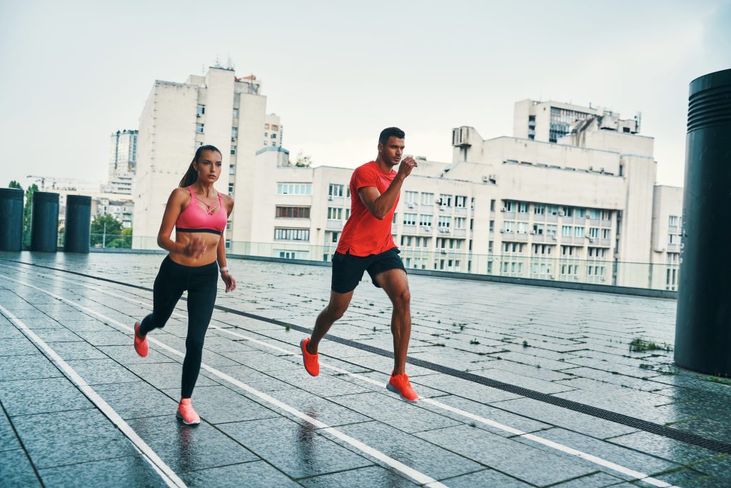 Full length of young man and woman in sports clothing jumping and jogging while exercising on the city street outdoors