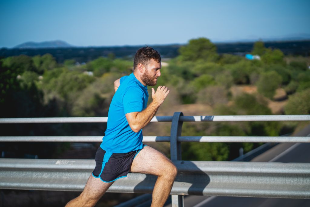 Young man takes a sprint over a highway bridge an hour before sunset surrounded by nature in Mallorca (Spain)