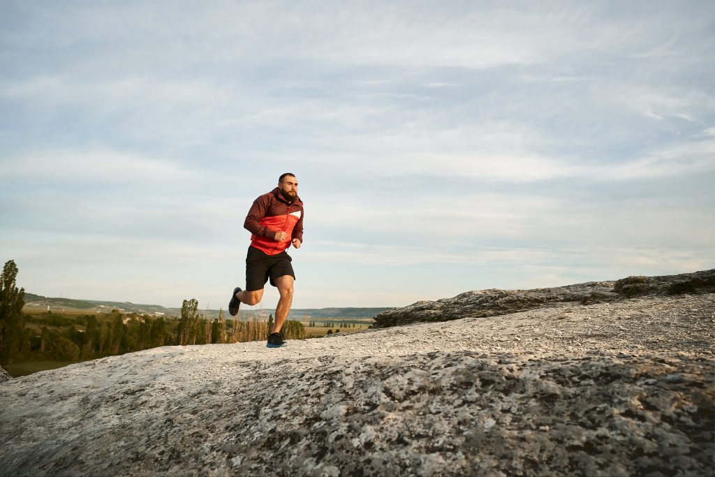 Young muscular male athlete running up the hill